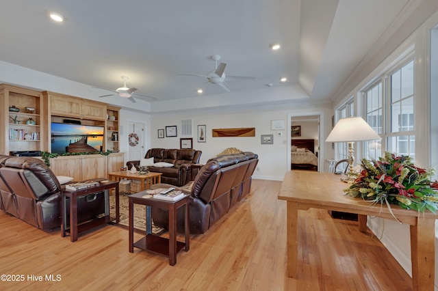 living room with light wood-type flooring, ceiling fan, and a raised ceiling