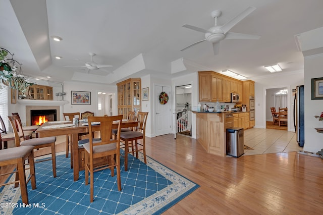 dining space with ceiling fan, light wood-type flooring, crown molding, and a raised ceiling