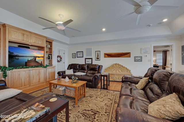 living room with ceiling fan, light hardwood / wood-style flooring, and a raised ceiling