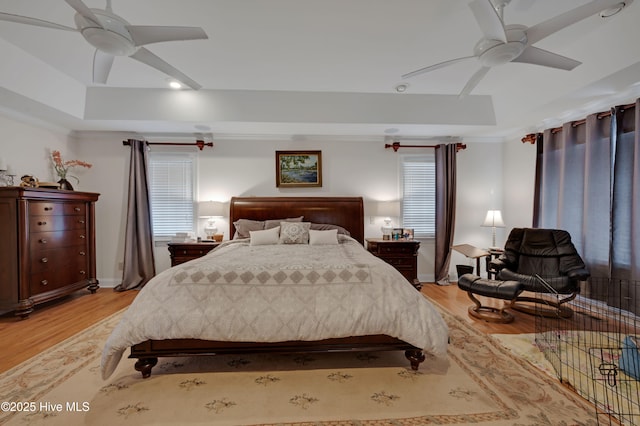 bedroom with ceiling fan, a tray ceiling, and light wood-type flooring