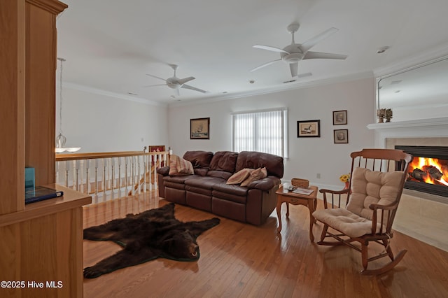 living room with ceiling fan, crown molding, a fireplace, and light hardwood / wood-style flooring