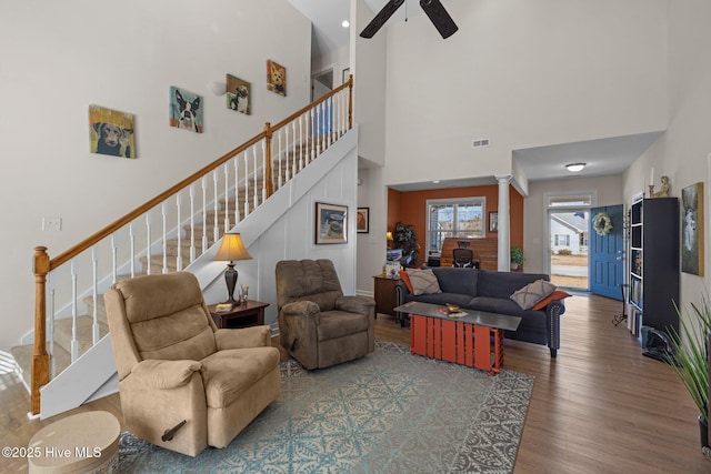 living room with ceiling fan, a towering ceiling, ornate columns, and hardwood / wood-style floors