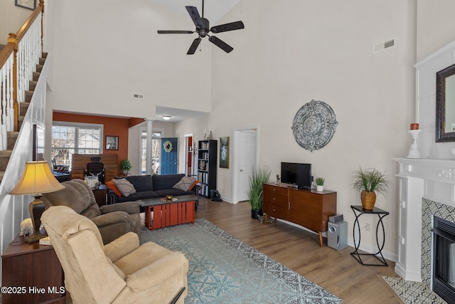 living room with hardwood / wood-style floors, a towering ceiling, ornate columns, ceiling fan, and a tiled fireplace