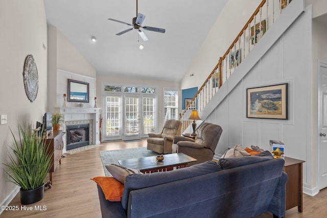 living room featuring ceiling fan, light hardwood / wood-style floors, high vaulted ceiling, and a fireplace