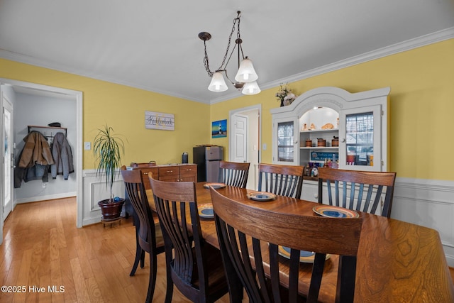 dining area featuring light hardwood / wood-style flooring, an inviting chandelier, built in features, and ornamental molding