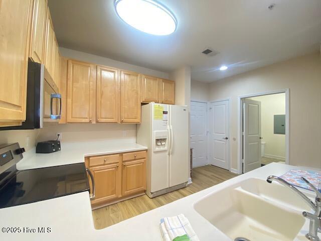 kitchen featuring light brown cabinets, stove, sink, white fridge with ice dispenser, and light hardwood / wood-style floors