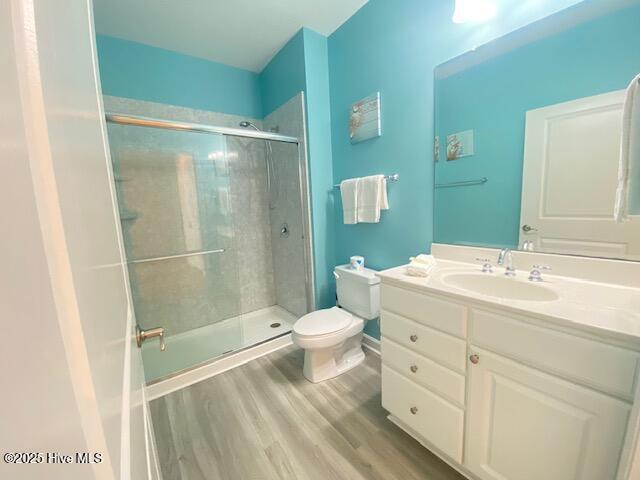 bathroom with toilet, wood-type flooring, a shower with shower door, and vanity