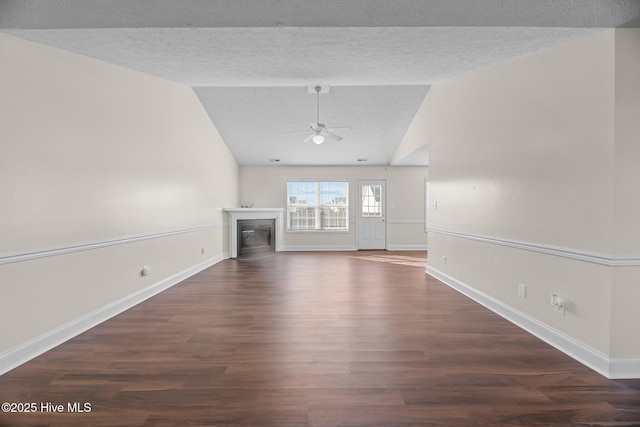 unfurnished living room featuring a textured ceiling, ceiling fan, dark wood-type flooring, and vaulted ceiling