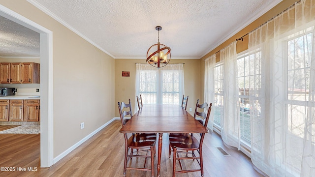 dining space featuring a textured ceiling, light hardwood / wood-style floors, an inviting chandelier, and crown molding