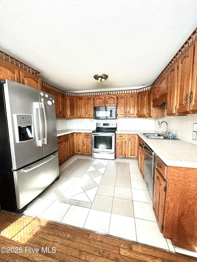 kitchen featuring sink, backsplash, stainless steel appliances, a textured ceiling, and light tile patterned flooring