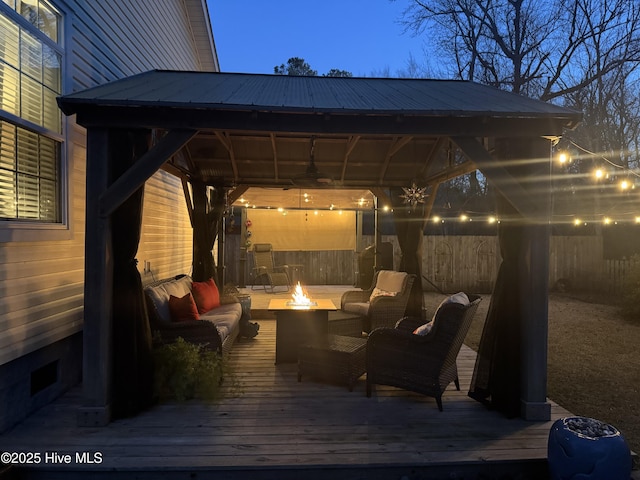 patio terrace at dusk with a fire pit, a wooden deck, and a gazebo