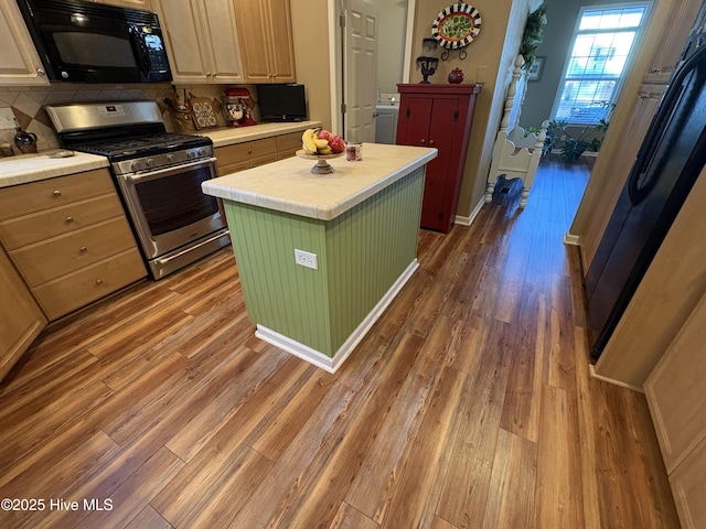 kitchen featuring stainless steel gas range, hardwood / wood-style flooring, tasteful backsplash, washer / dryer, and a kitchen island