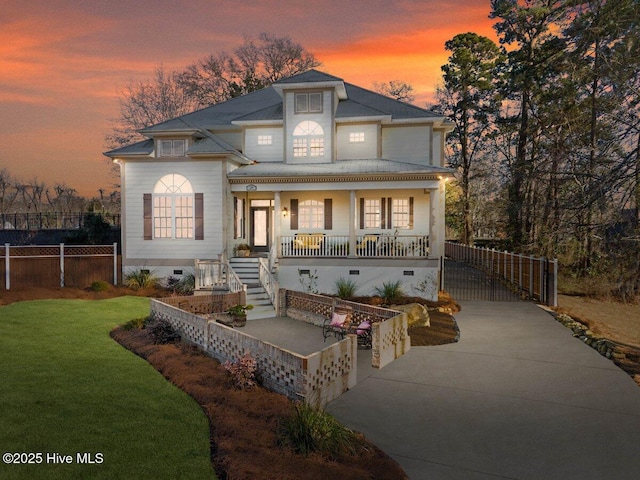 back house at dusk featuring covered porch and a yard