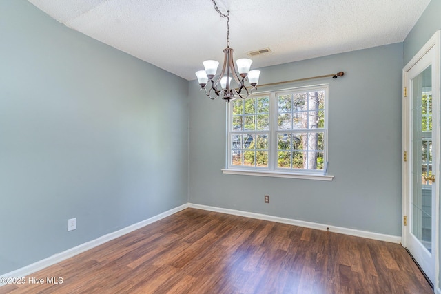 empty room with a notable chandelier, dark hardwood / wood-style floors, and a textured ceiling