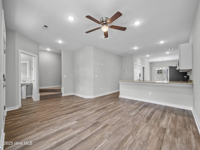 unfurnished living room featuring ceiling fan with notable chandelier, sink, and light hardwood / wood-style floors