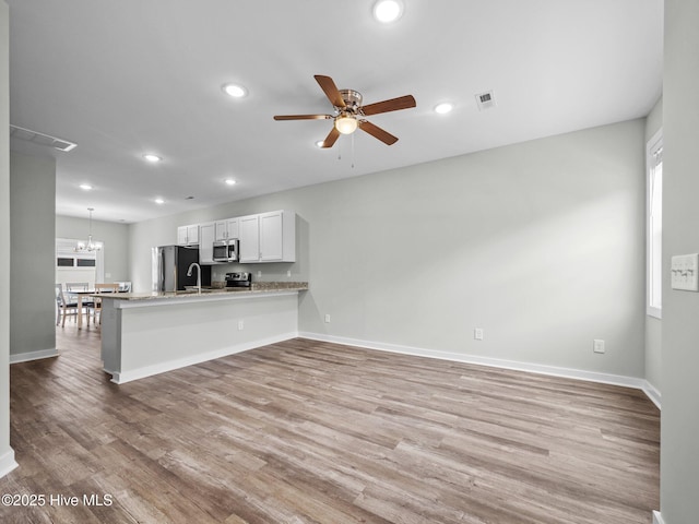 interior space featuring kitchen peninsula, light hardwood / wood-style floors, stainless steel appliances, ceiling fan with notable chandelier, and white cabinets