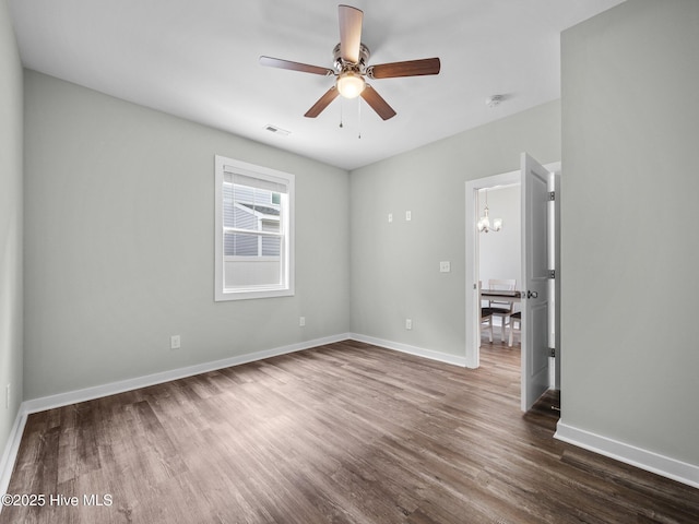 empty room with dark hardwood / wood-style flooring and ceiling fan with notable chandelier