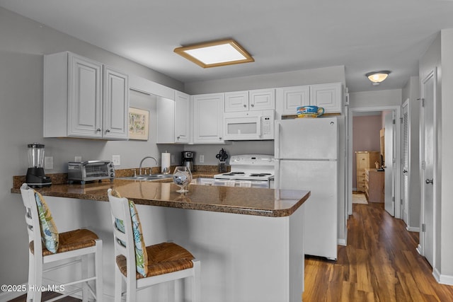 kitchen with kitchen peninsula, a breakfast bar, white cabinets, and white appliances