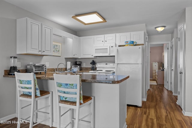 kitchen featuring a kitchen breakfast bar, dark hardwood / wood-style flooring, kitchen peninsula, white appliances, and white cabinets