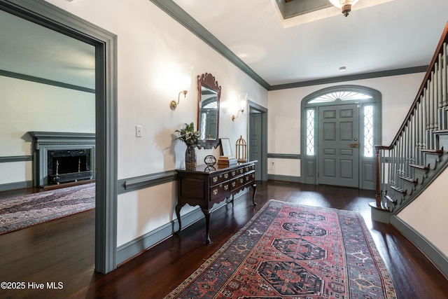 entryway with a fireplace, dark wood-type flooring, and ornamental molding