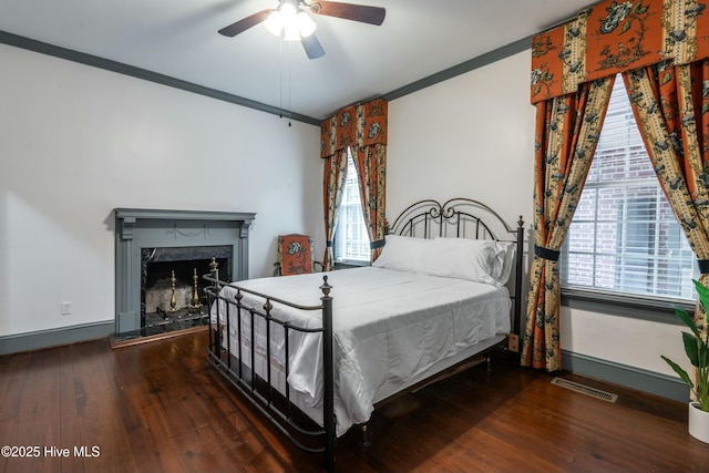 bedroom with a fireplace, crown molding, dark wood-type flooring, and ceiling fan