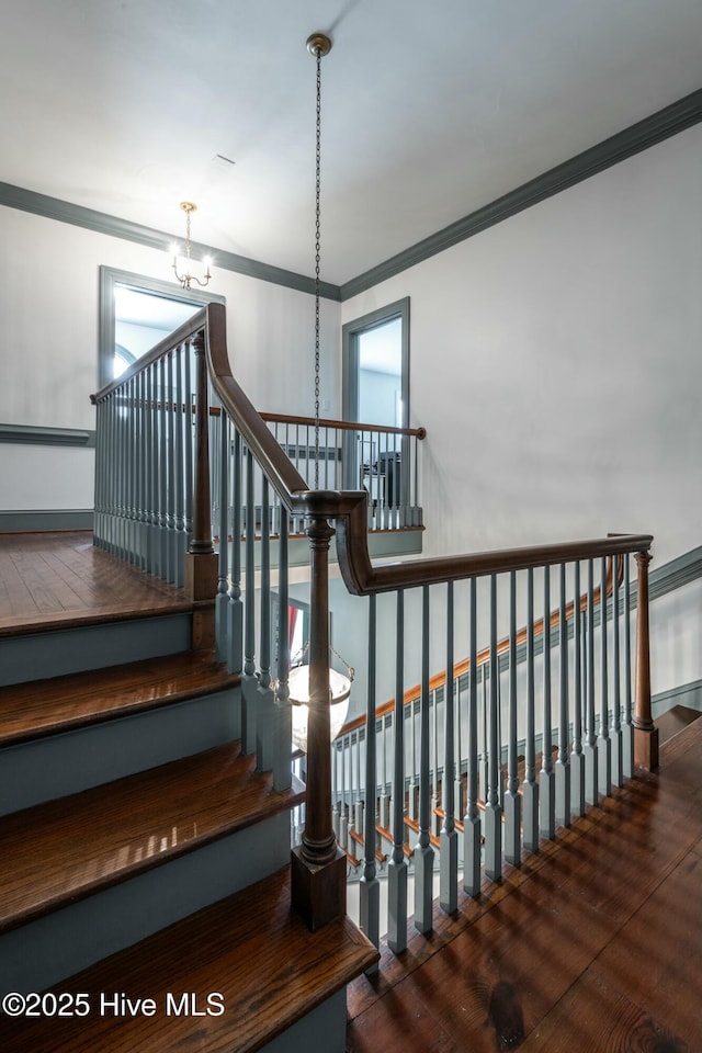 stairway with an inviting chandelier, crown molding, and hardwood / wood-style flooring