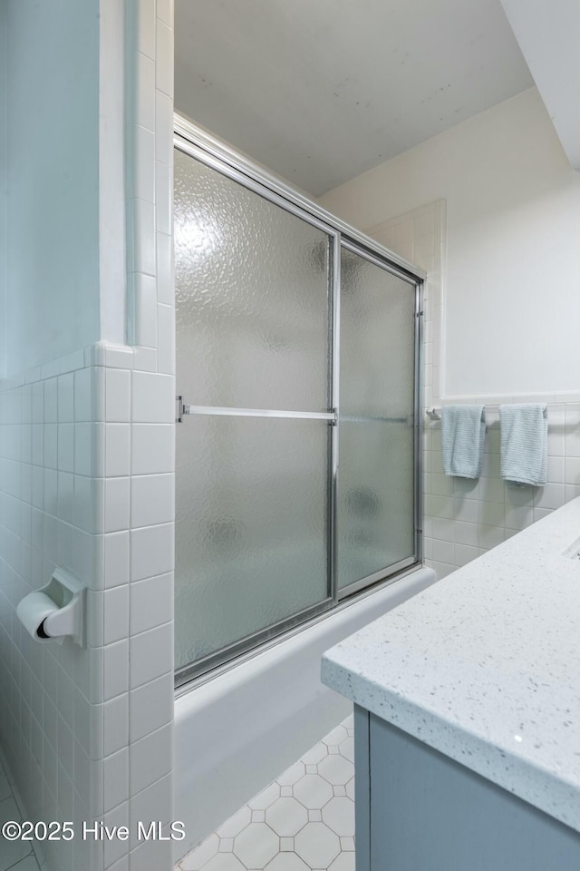 bathroom with tile walls, tile patterned flooring, and combined bath / shower with glass door