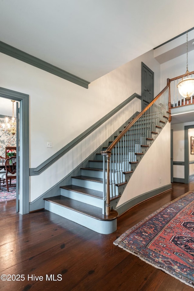 stairway featuring hardwood / wood-style flooring, crown molding, and a chandelier