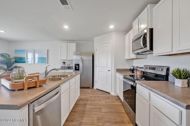 kitchen featuring stainless steel appliances, recessed lighting, light wood-style floors, white cabinetry, and a sink