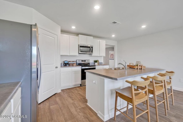 kitchen with stainless steel appliances, sink, light hardwood / wood-style floors, white cabinetry, and a breakfast bar area