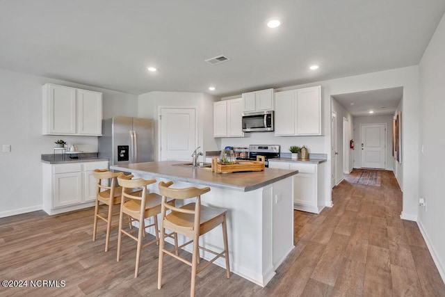 kitchen featuring a breakfast bar, a center island with sink, white cabinets, and stainless steel appliances