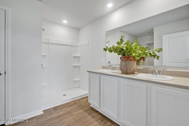 bathroom with a stall shower, double vanity, a sink, and wood finished floors