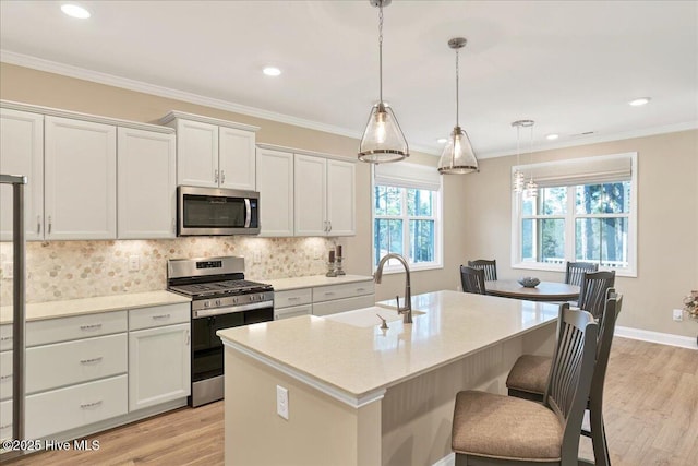 kitchen featuring stainless steel appliances, sink, white cabinetry, hanging light fixtures, and an island with sink