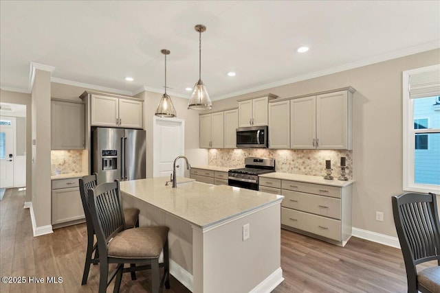 kitchen with decorative backsplash, appliances with stainless steel finishes, wood-type flooring, hanging light fixtures, and an island with sink