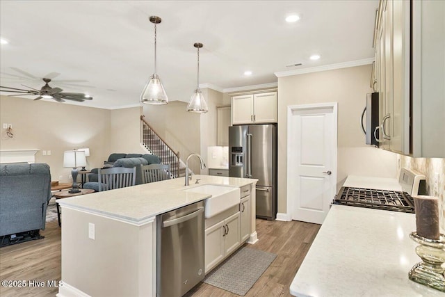 kitchen featuring sink, hanging light fixtures, stainless steel appliances, hardwood / wood-style floors, and a center island with sink