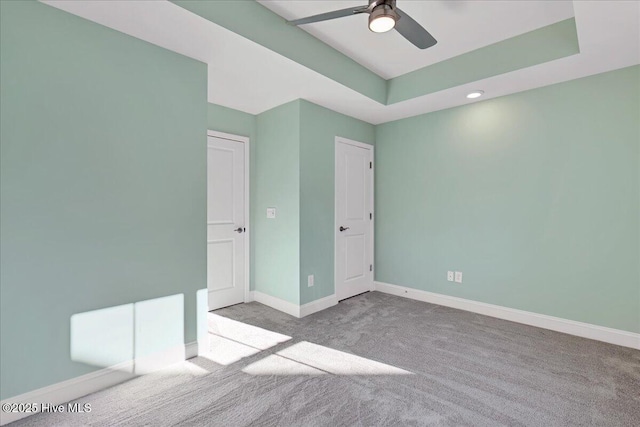 unfurnished bedroom with light colored carpet, ceiling fan, and a tray ceiling