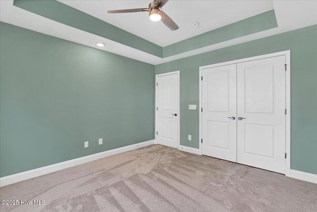 unfurnished bedroom featuring carpet, ceiling fan, a raised ceiling, and a closet