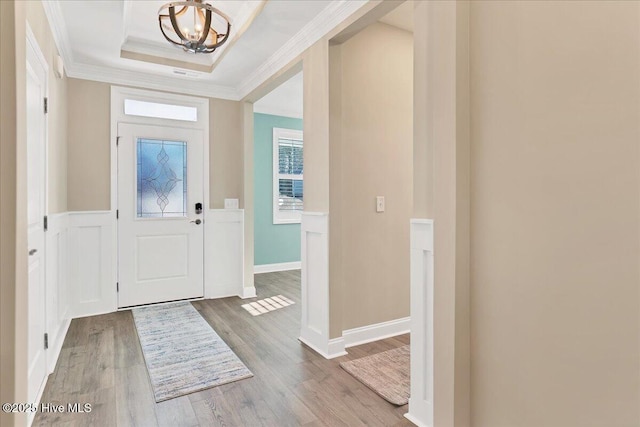 entryway with a raised ceiling, hardwood / wood-style flooring, a chandelier, and ornamental molding