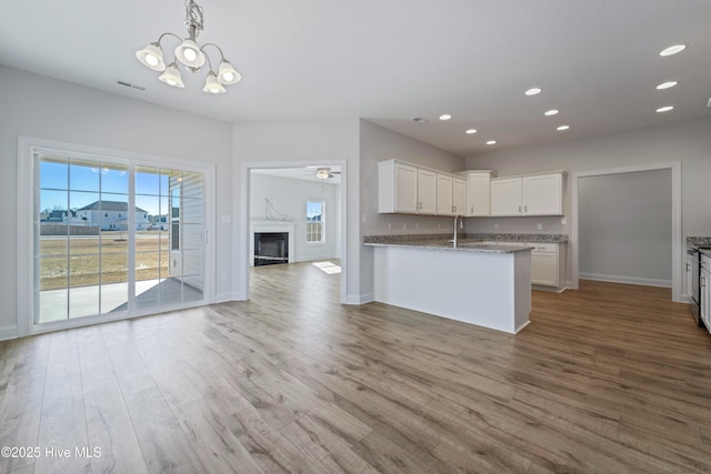 kitchen with stone counters, wood-type flooring, sink, hanging light fixtures, and white cabinets