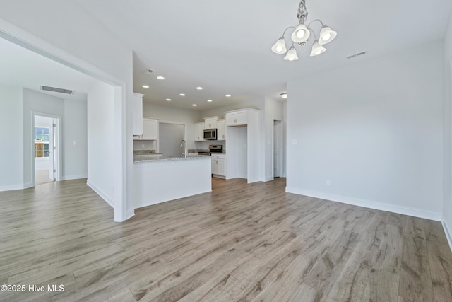 unfurnished living room with sink, a notable chandelier, and light wood-type flooring