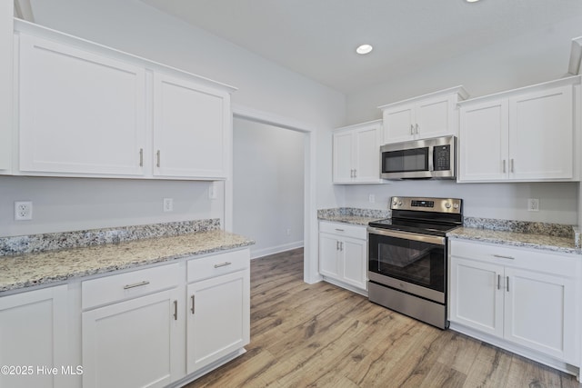 kitchen with light stone countertops, appliances with stainless steel finishes, white cabinetry, and light hardwood / wood-style flooring