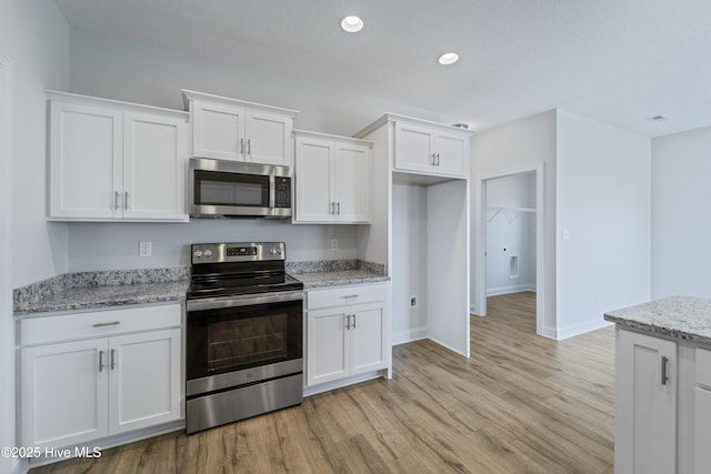 kitchen with appliances with stainless steel finishes, light stone counters, and white cabinetry