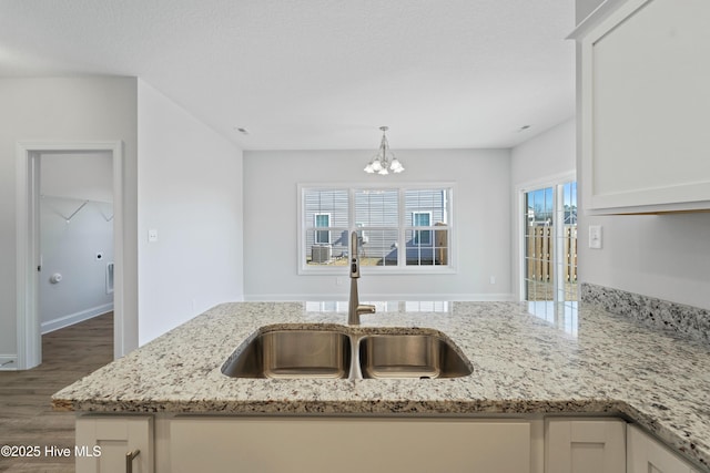 kitchen featuring white cabinets, sink, hanging light fixtures, a notable chandelier, and light stone counters