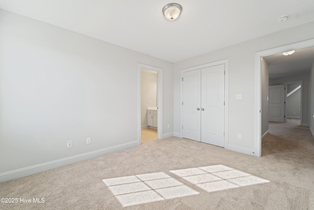 unfurnished bedroom with ensuite bath, light colored carpet, and a closet