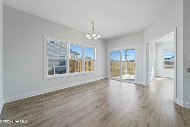 unfurnished dining area featuring light hardwood / wood-style floors, plenty of natural light, a textured ceiling, and an inviting chandelier