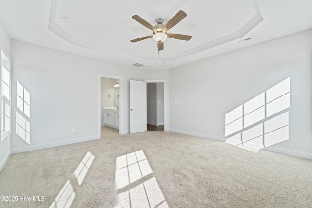 unfurnished bedroom with light carpet, ceiling fan, connected bathroom, and a tray ceiling