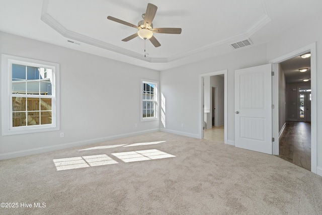 carpeted empty room featuring ceiling fan, a wealth of natural light, a tray ceiling, and crown molding