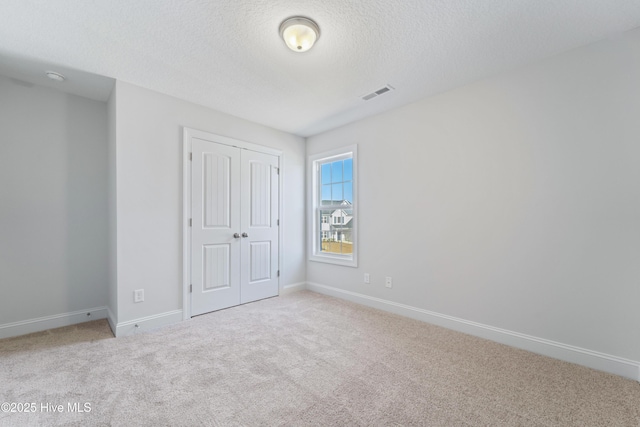 unfurnished bedroom with a textured ceiling, a closet, and light carpet