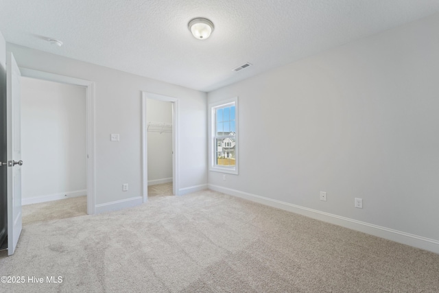 unfurnished bedroom featuring light colored carpet, a closet, a spacious closet, and a textured ceiling