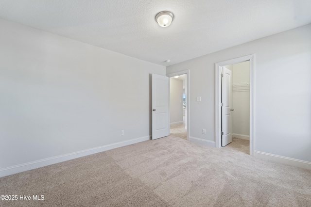 unfurnished bedroom with a spacious closet, a closet, a textured ceiling, and light colored carpet